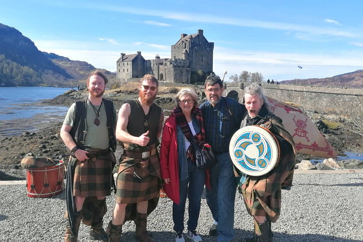 A family with kilted pipers and a drummer in front of Eilean Donan Castle